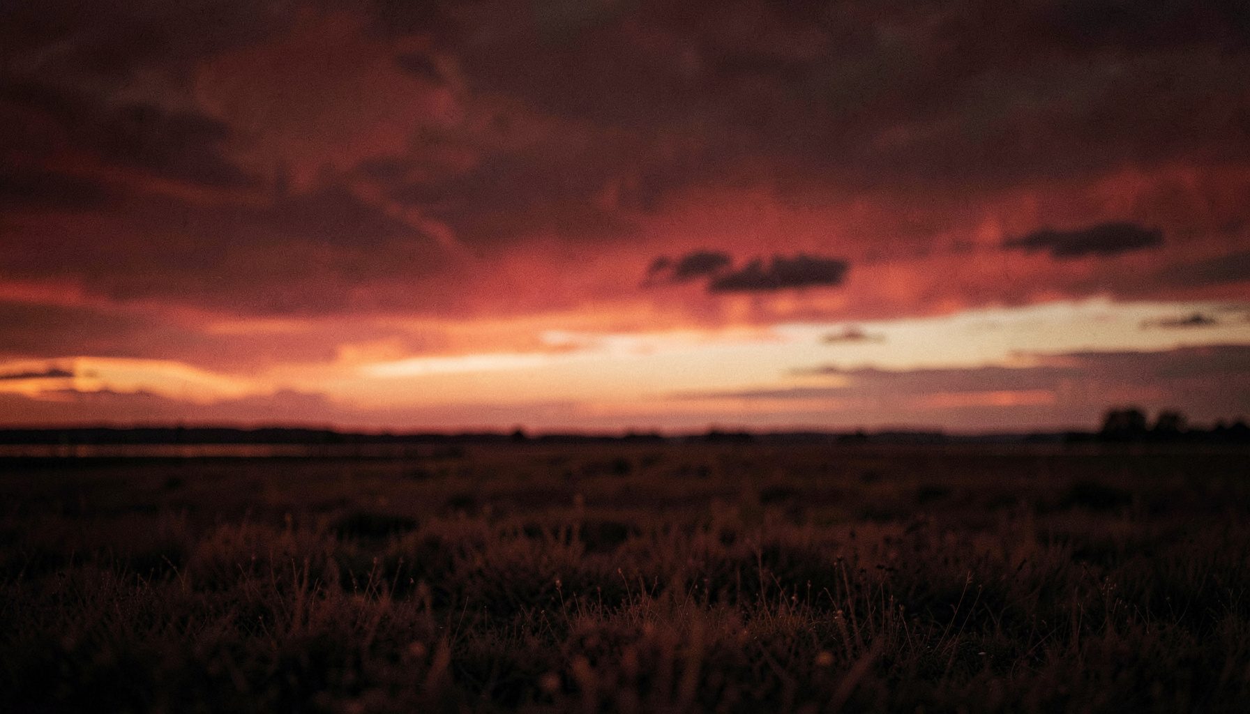 Ciel crépusculaire aux teintes rouge sombre et crème au-dessus d'une plaine silencieuse, mise au point douce, ambiance paisible